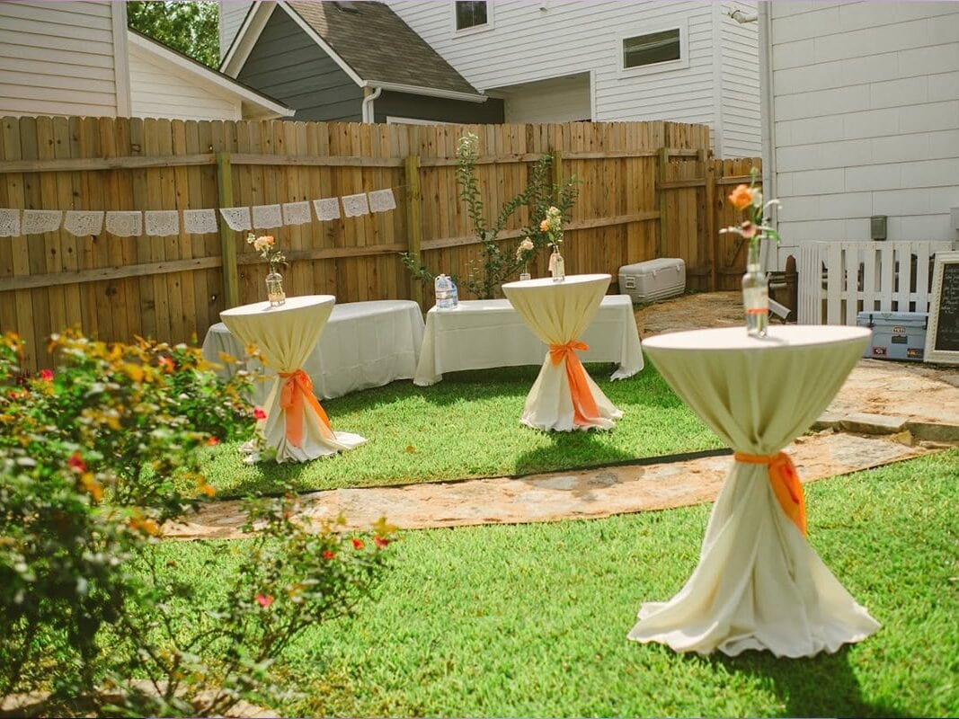 White hourglass cocktail tables in backyard with orange bows and flowers at Austin wedding
