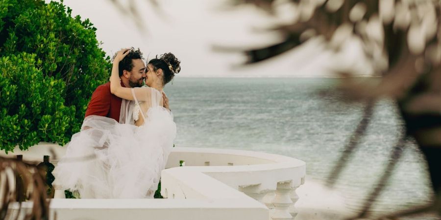Bride and groom embracing by the ocean after their ceremony, highlighting how to plan a destination wedding on a small budget in a tropical location.