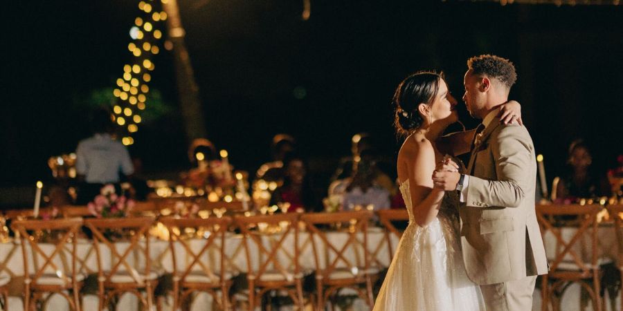 Bride and groom sharing their first dance under string lights at an outdoor reception, capturing how long does it take to plan a destination wedding for a magical evening.