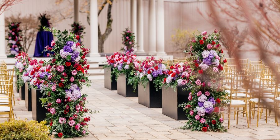 Outdoor wedding ceremony aisle decorated with colorful floral arrangements, showcasing inspiration for an event planning business plan. Planned by Tyler Reid of Eminent Events. Photography by Forever Photography by Stanlo Photography.