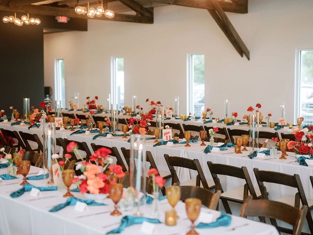 Indoor Houston wedding planner designed with long white tables, wood chairs, colorful flowers on table