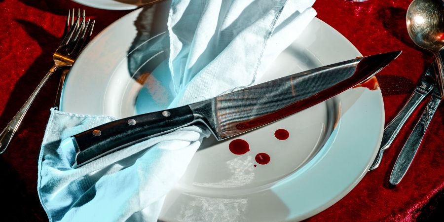 DIY Halloween food party ideas with a spooky place setting featuring a bloody knife prop on a dinner plate for a themed table display.