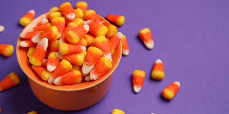 DIY Halloween food party ideas featuring a bowl of classic candy corn on a purple background for a festive snack display.