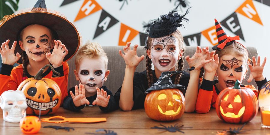 Kid-friendly Halloween party ideas with children in costumes posing with carved pumpkins and spooky decorations.