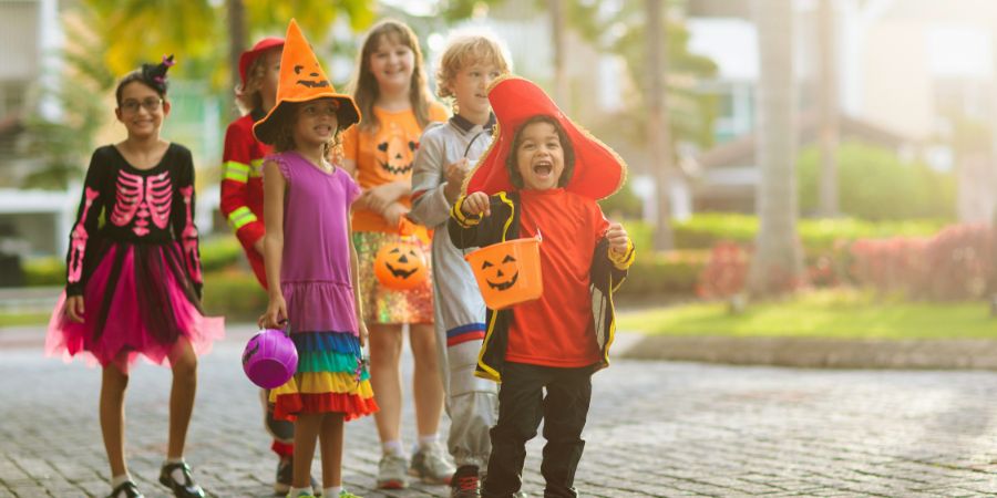 Halloween party games for kids with a group of children in colorful costumes trick-or-treating together outdoors.