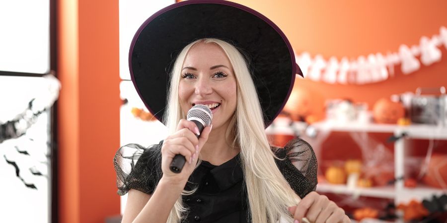 Halloween party ideas for adults featuring a woman in a witch costume singing karaoke at a festive celebration.