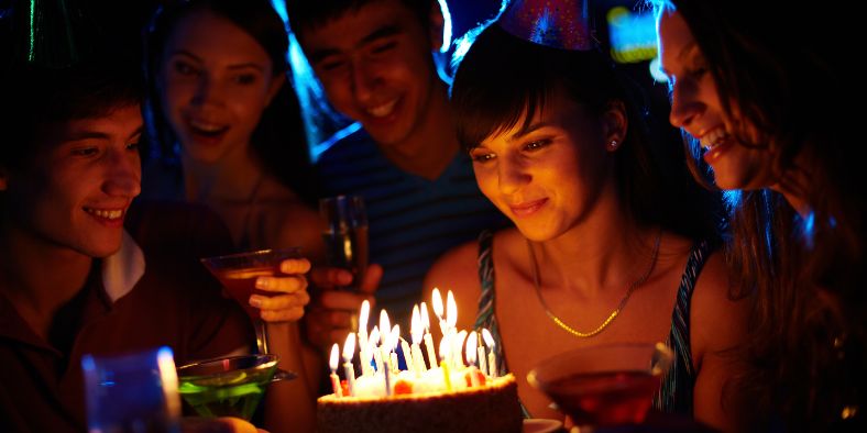 Group of teenagers celebrating around a birthday cake with candles, showing how to plan a birthday party for teenagers with fun and memorable moments.