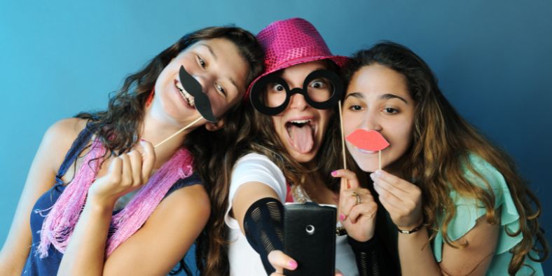 Teenagers taking fun selfies with photo booth props, showing creative birthday party activities to make the celebration memorable.