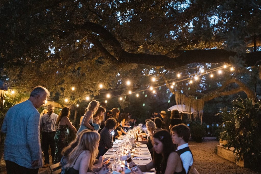 Outdoor Tampa wedding with long table, string lights on tree, guests eating