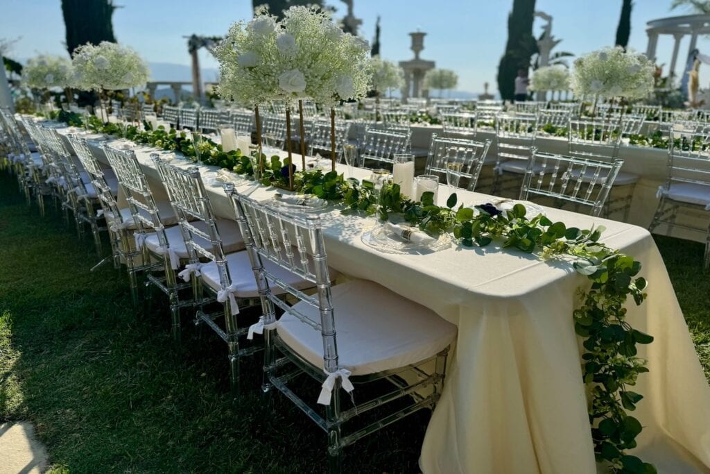Long banquet tables set up outside decorated with garlands of greenery and large all-white centerpieces