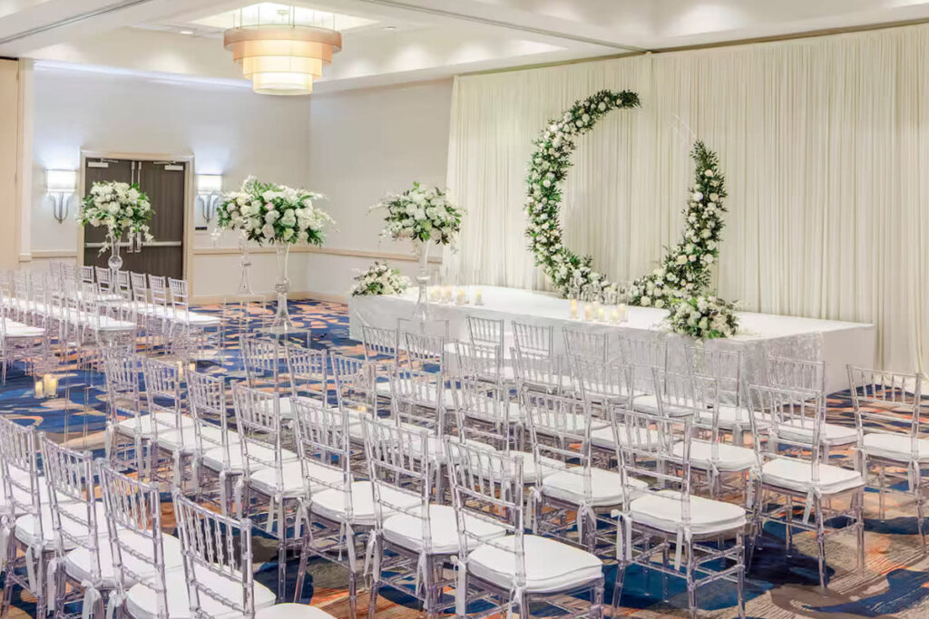 Indoor LA wedding venue with clear plastic chairs facing a semi-circle floral arch