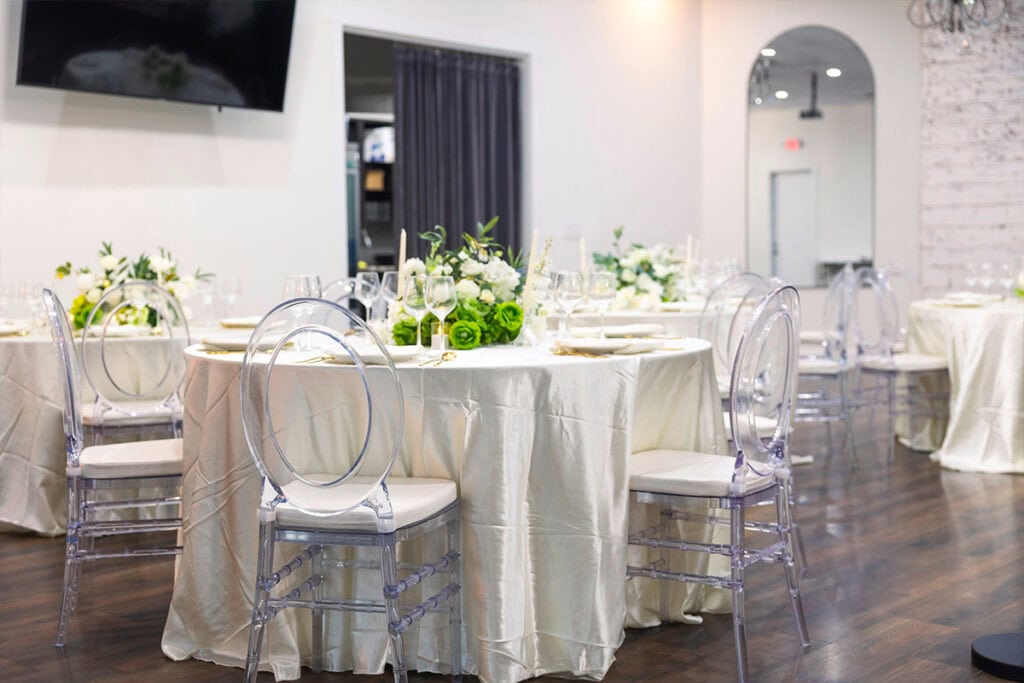 Indoor Los Angeles wedding dinner area with clear chairs, round tables with white tablecloth, glorals