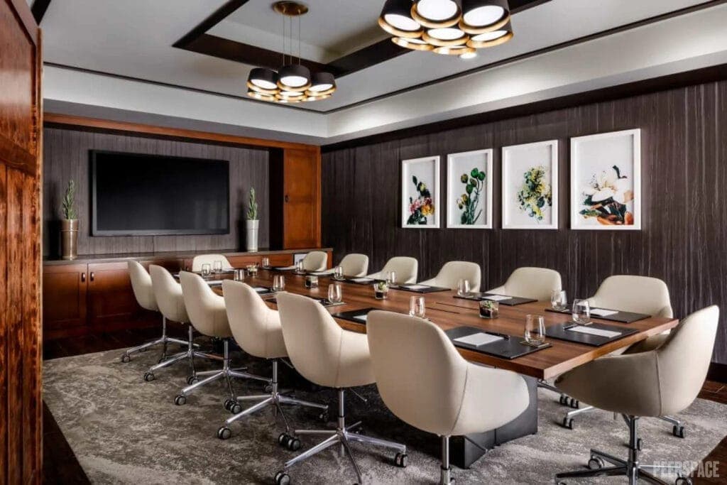 A modern boardroom with dark wood features and white chairs is set up for a meeting