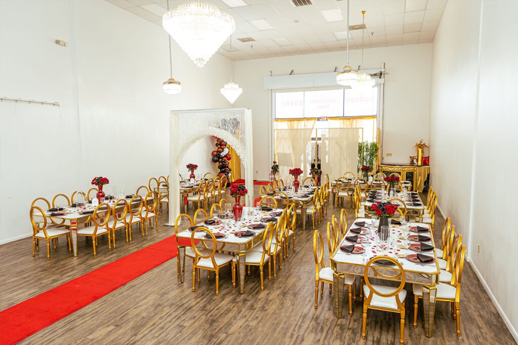 Indoor Los Angeles wedding planned with long wood tables, chairs, red roses, and chandeliers