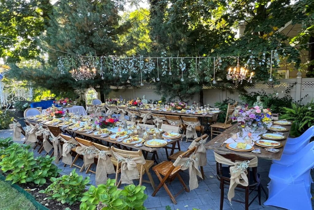 Burlap and babies breath decorate wooden folding chairs at a small, boho-chic reception set up outside in a garden surrounded by pine trees
