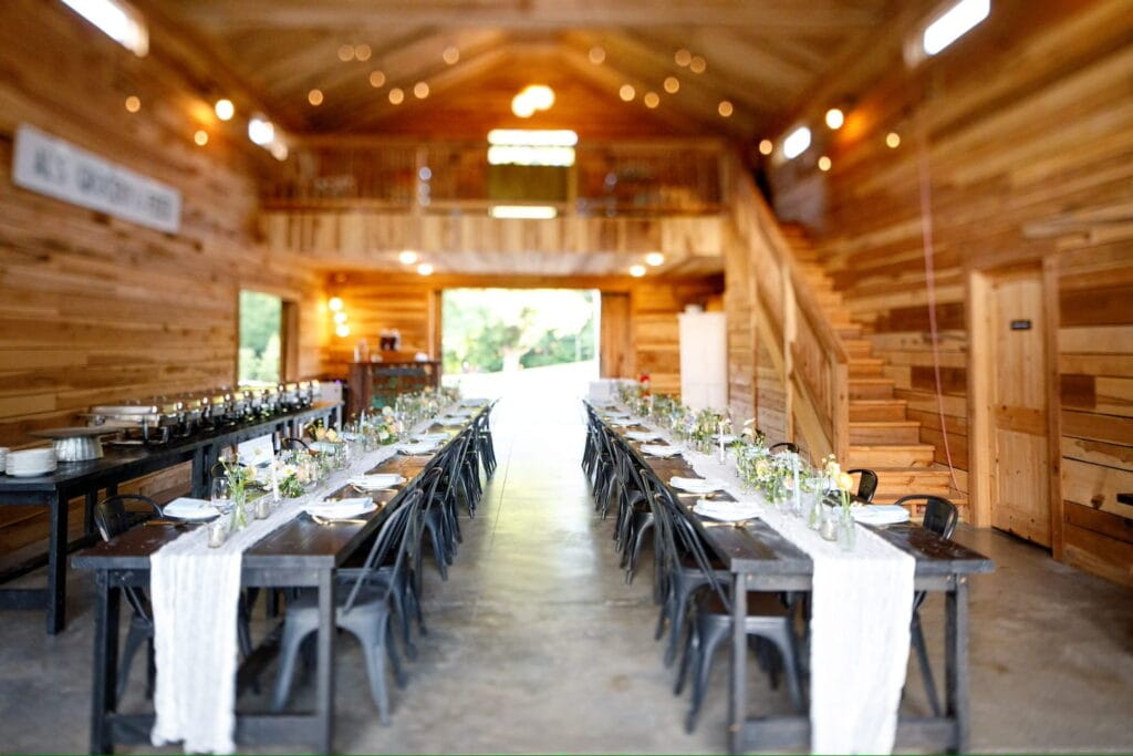 Long wooden tables and black metal chairs create a wedding reception space inside a large wooden barn