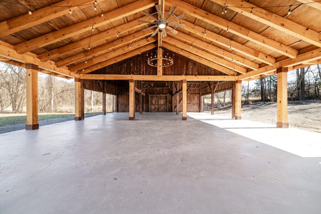 A large open-air pavilion is strung with bistro lights and chandeliers in a field