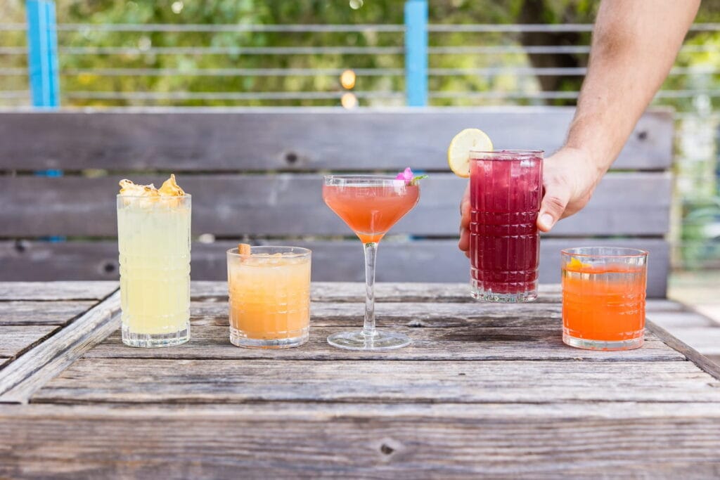 A selection of colorful cocktails sit on a wooden outdoor bar