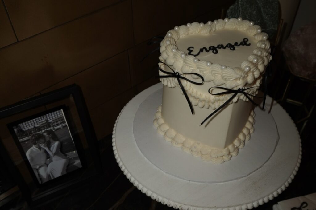 A white cake with black writing and ribbons that says "engaged" in frosting
