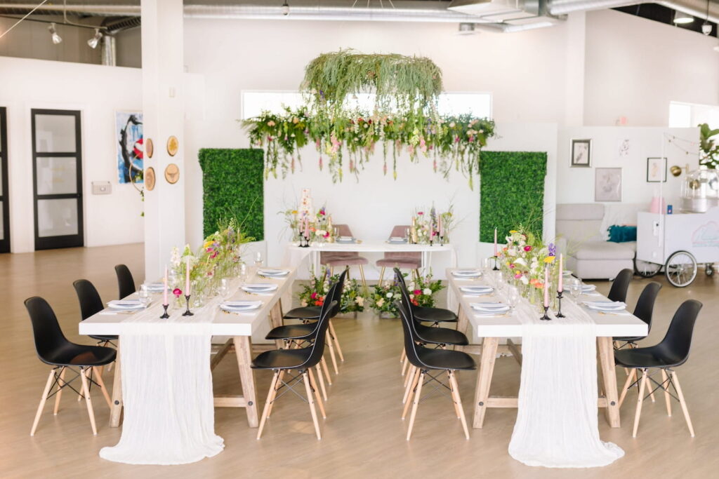 An all-white event space is punctuated but lush greenery and wildflowers hanging from the ceiling and decorating the tables