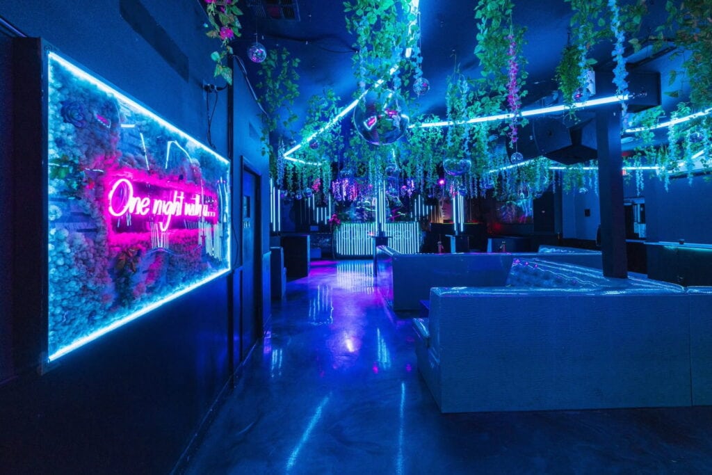 Neon lights highlight a club space in Las Vegas with greenery and disco balls hanging from the ceiling
