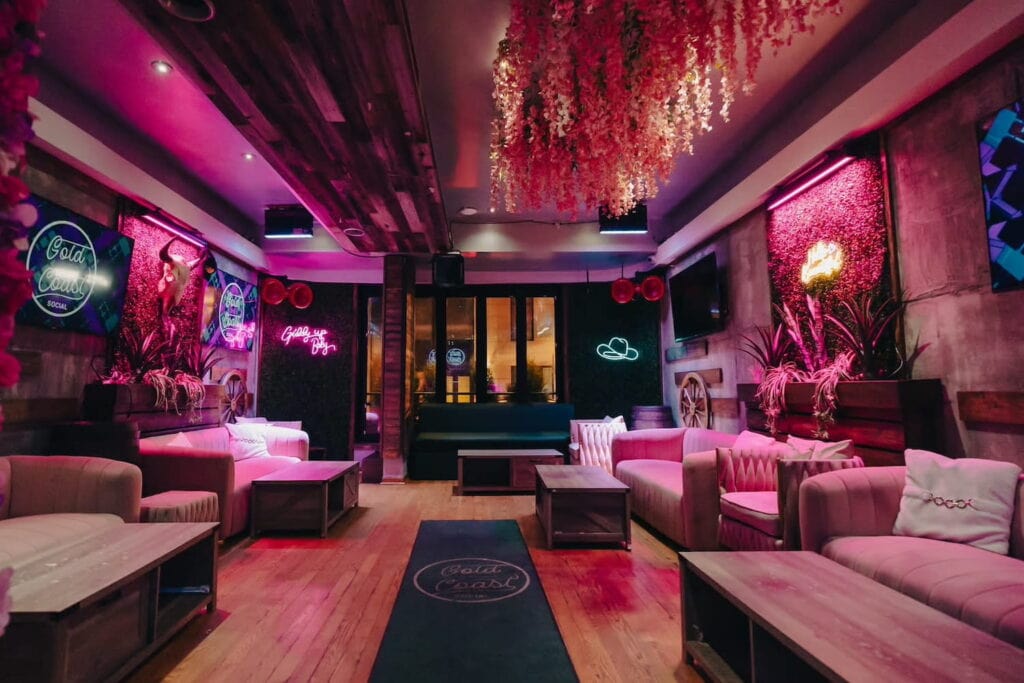 Neon lights and signs illuminate a lounge space with brightly-colored walls and velvet couches