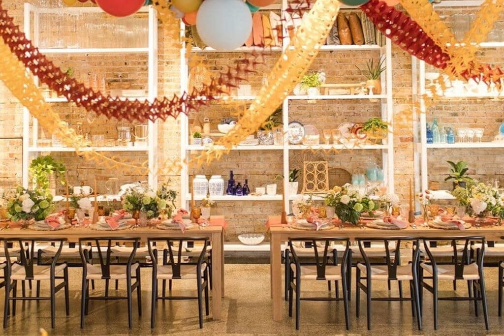 Two long tables are set up under colorful decor and balloons and decorated with lush flower arrangements and sweet table settings