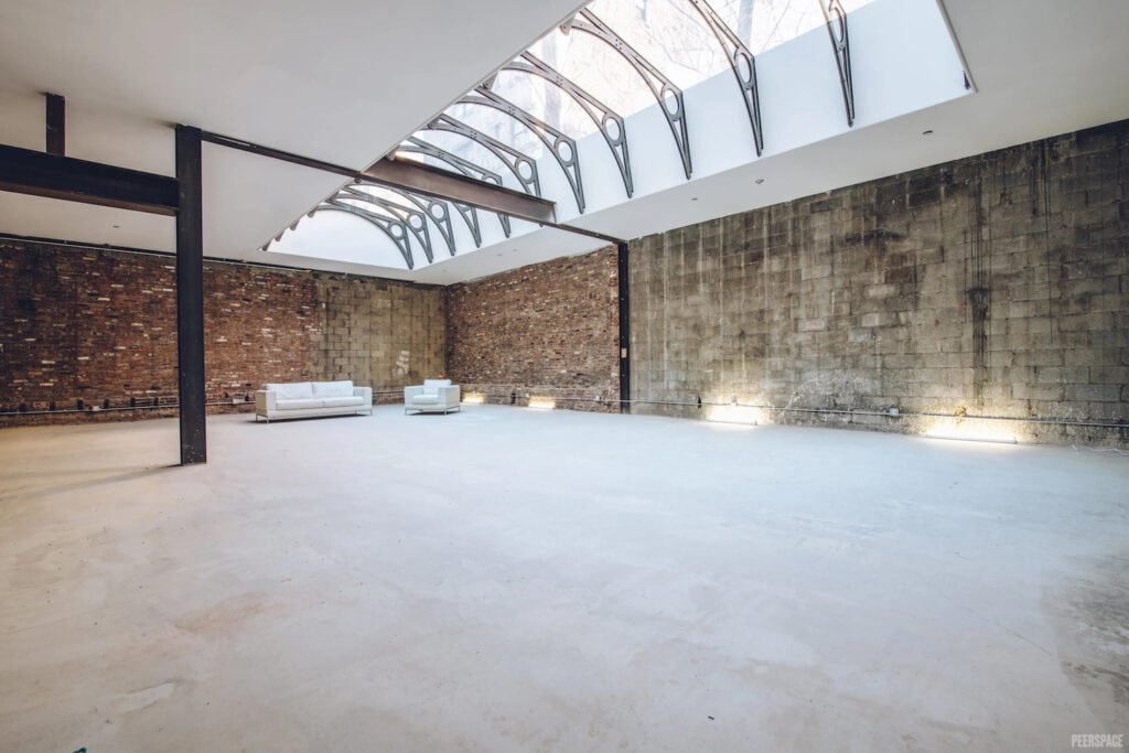 Wide-open warehouse space lit by huge skylight with a couch and chair