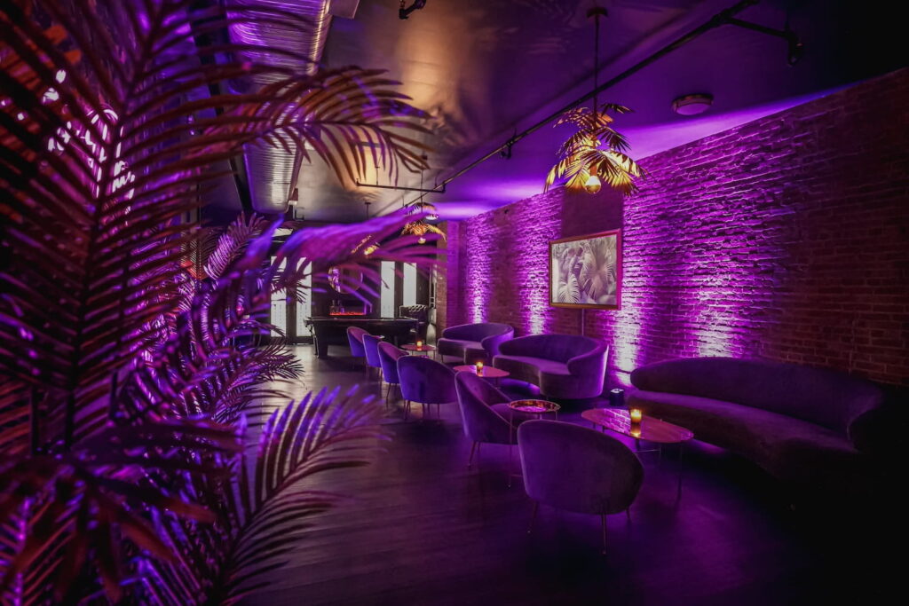 A New York City lounge space with brick walls and moody decor illuminated by purple neon lights