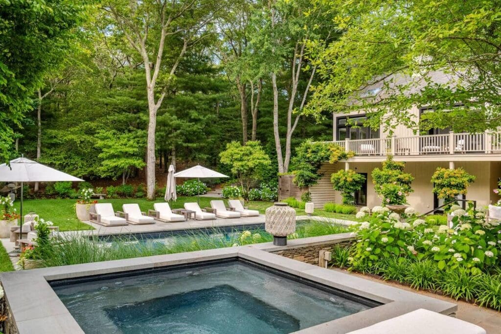 A lush Hamptons backyard with a pool, lounge chairs and loads of greenery