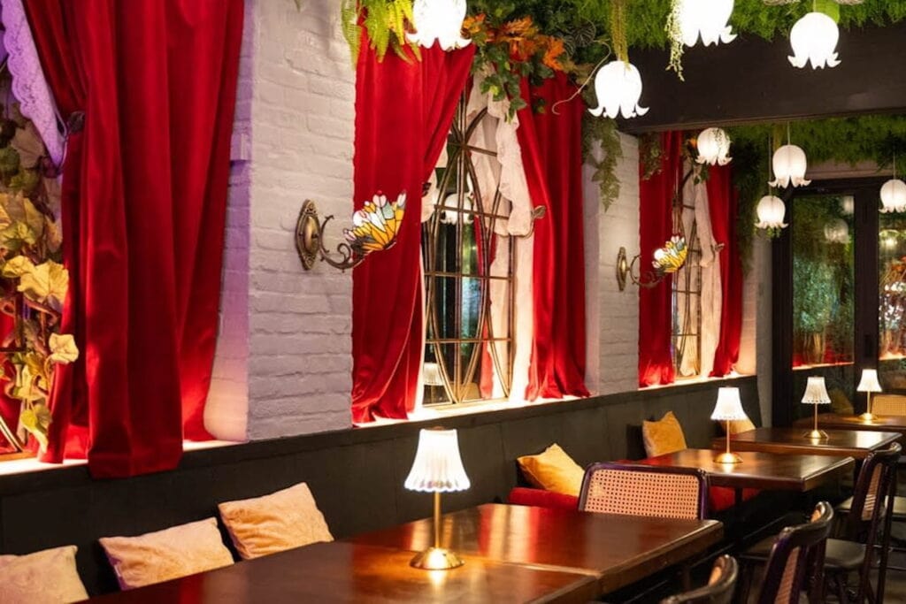 Red velvet drapes hang next to large mirrors in a moody New York City dining area lit by colorful, butterfly-shaped sconces and small table lamps