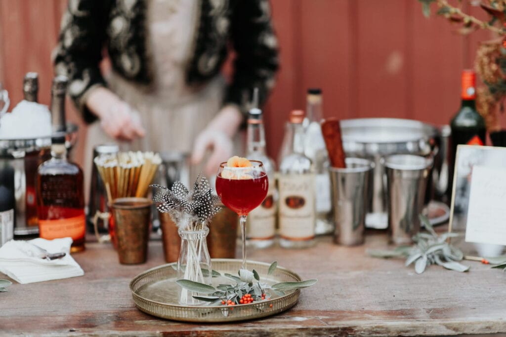 A red-hued signature drink sits on a metal platter at an outside bar