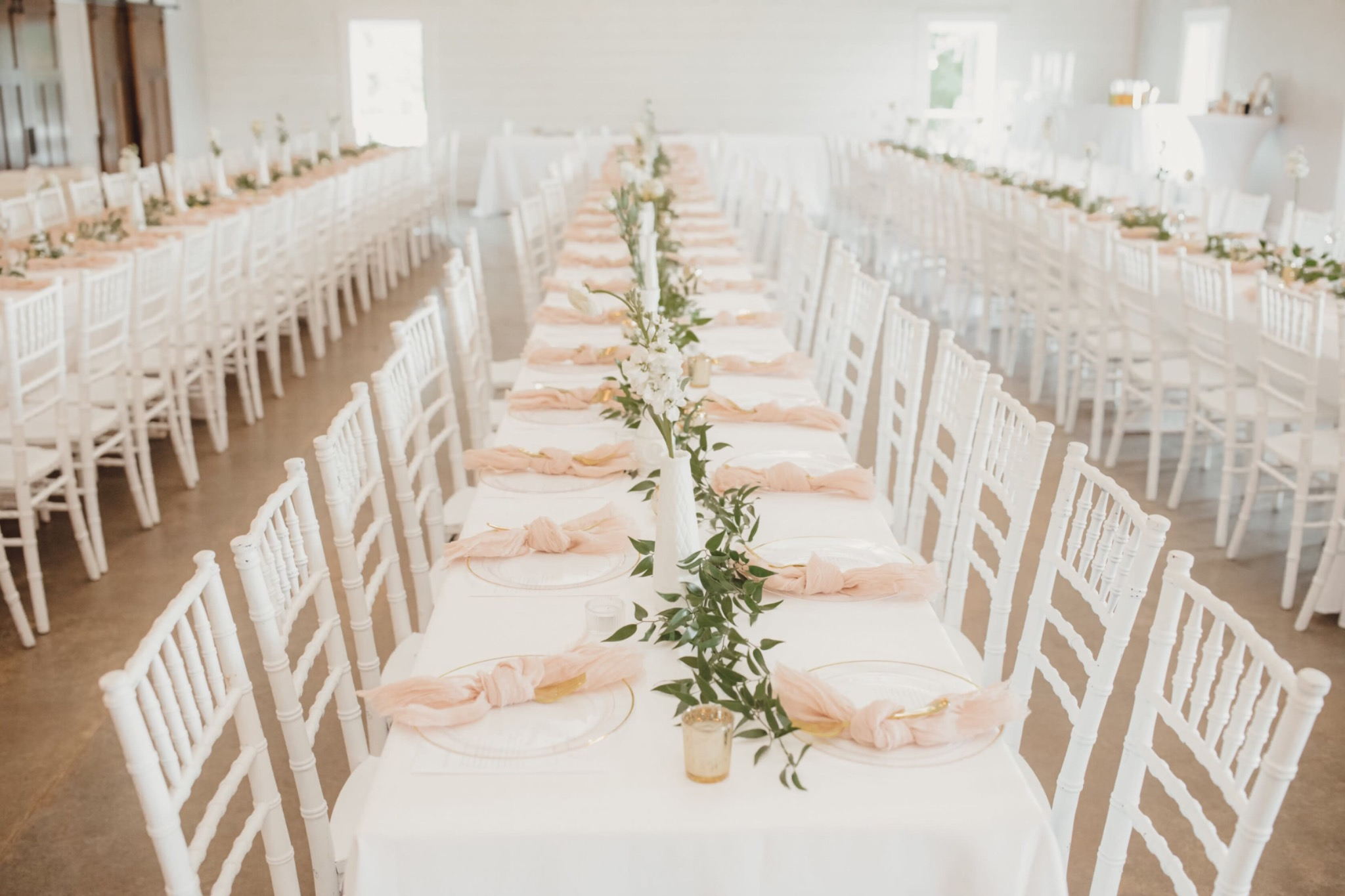 Elegant indoor Oklahoma wedding reception setup with white chairs and greenery