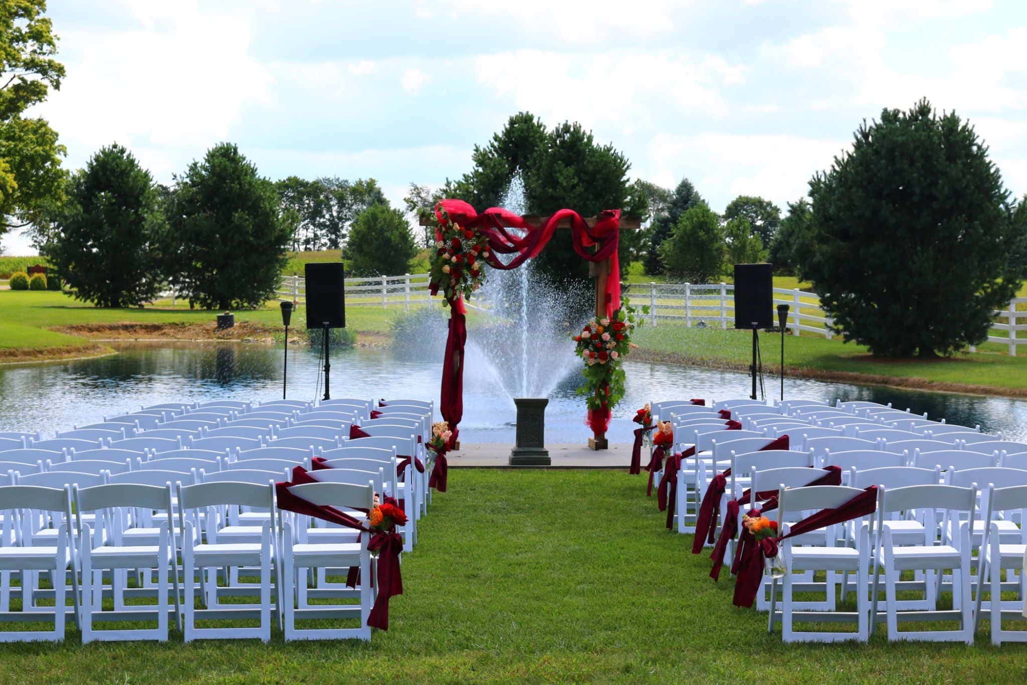 Outdoor Oklahoma wedding ceremony setup featuring red arch and fountain backdrop
