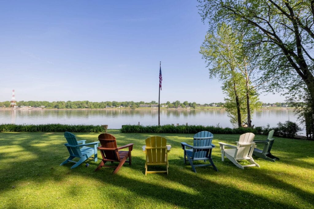 Colorful Adirondack chairs sit in the grass looking out over a lake