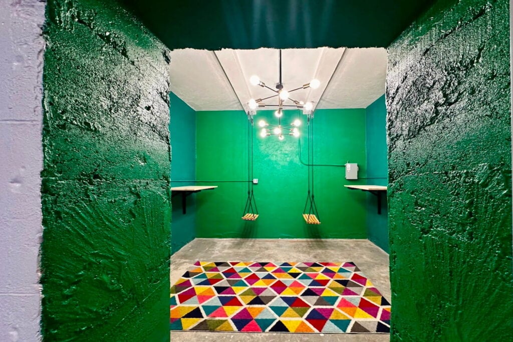 Two wooden swings hang from the ceiling in a small green exhibit room at an art gallery in San Bernadino