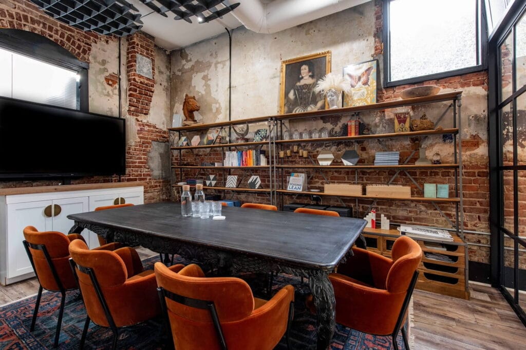 A meeting room with partially exposed brick walls, a large industrial bookshelf and large TV