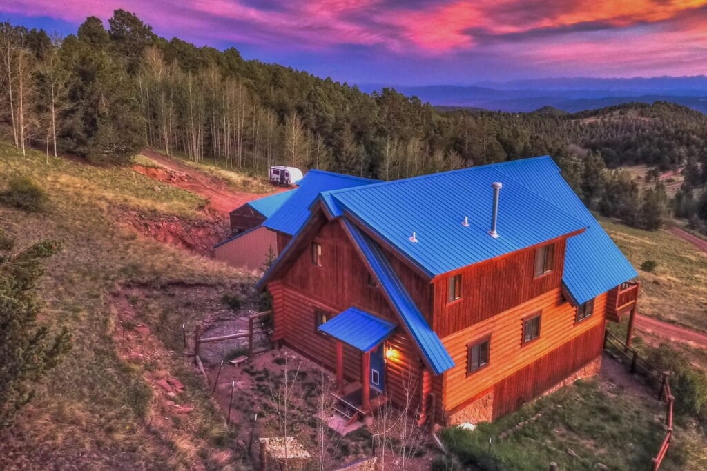 Mountainside wood cabin set in Colorado woods with sun setting over rolling hills
