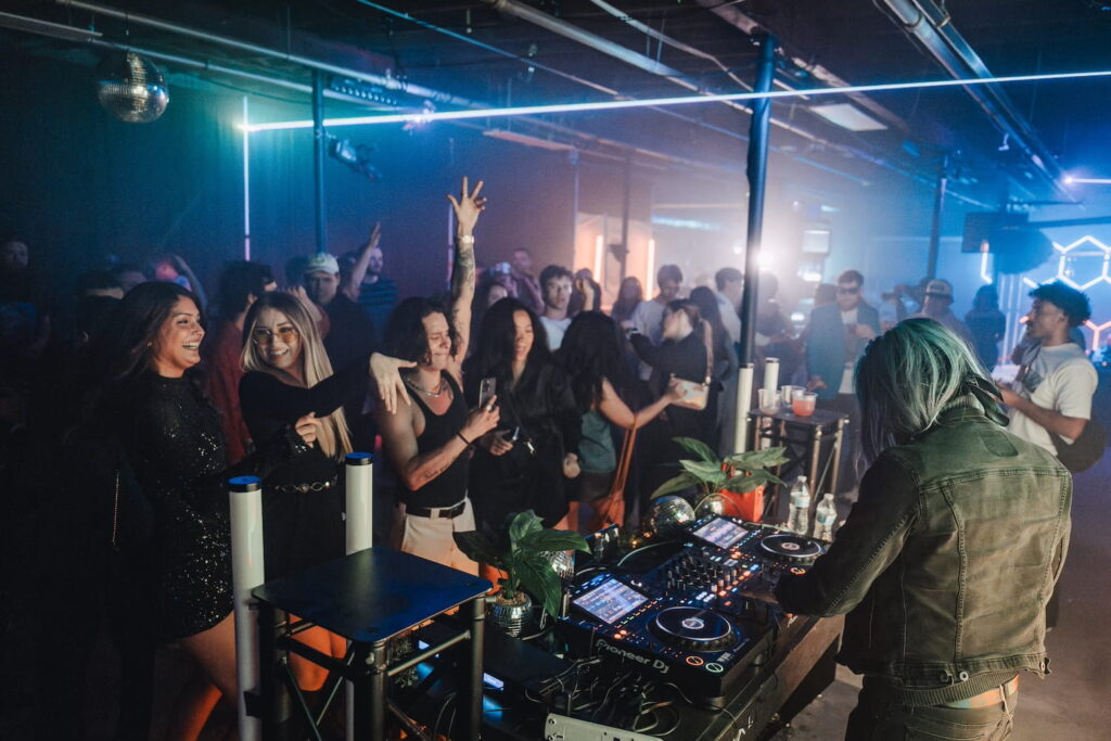 People dancing in a warehouse event space by a DJ table