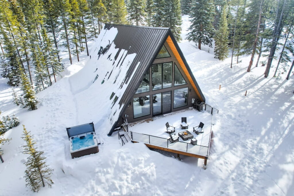 A-frame cabin with a hot tub nestled in the snowy trees of the Colorado mountainside