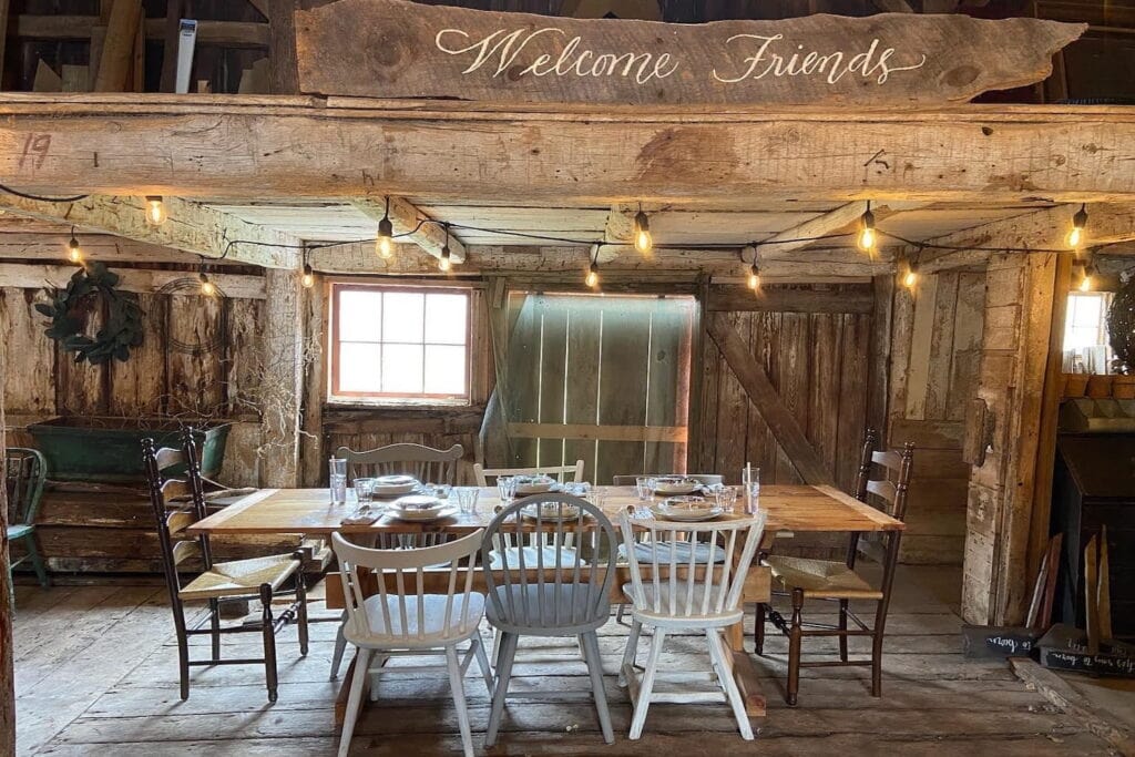 A dining room in a rustic and historic New England home with mismatched chairs around a wooden table under string lights
