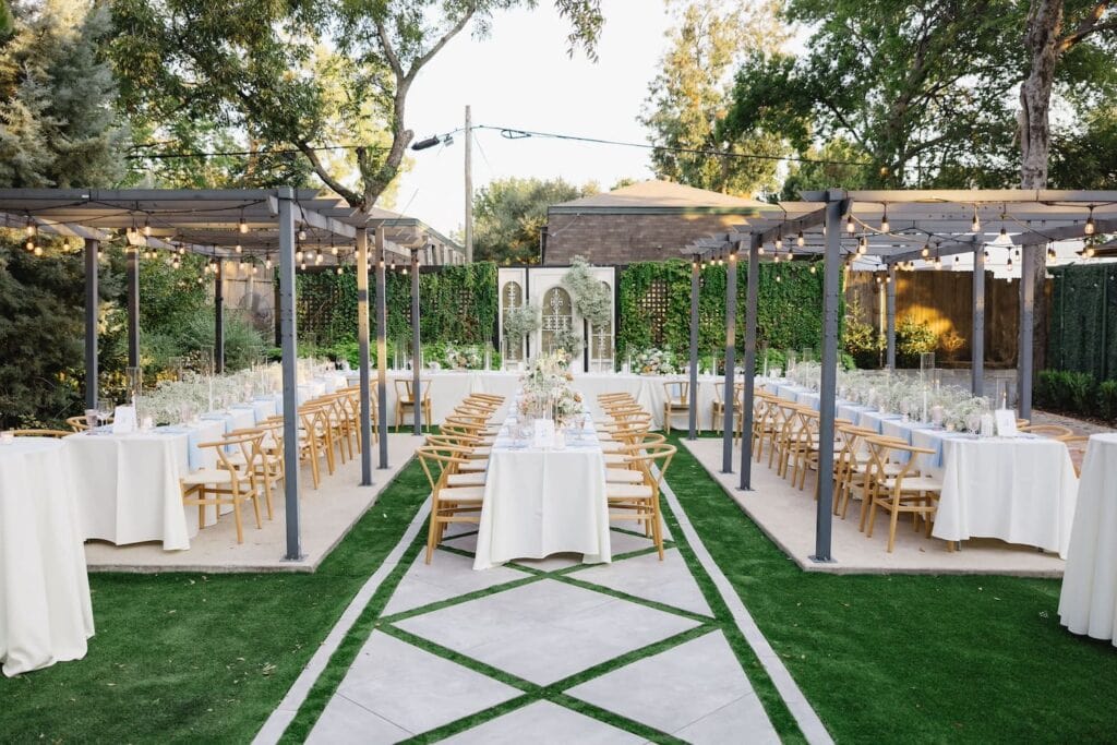 And outdoor dinner reception under wooden pergolas and surrounded by greenery