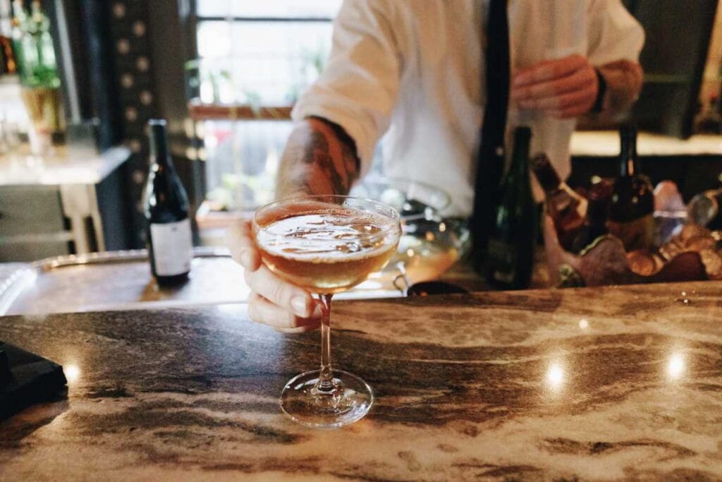 A bartender passes a cocktail across a marble bar