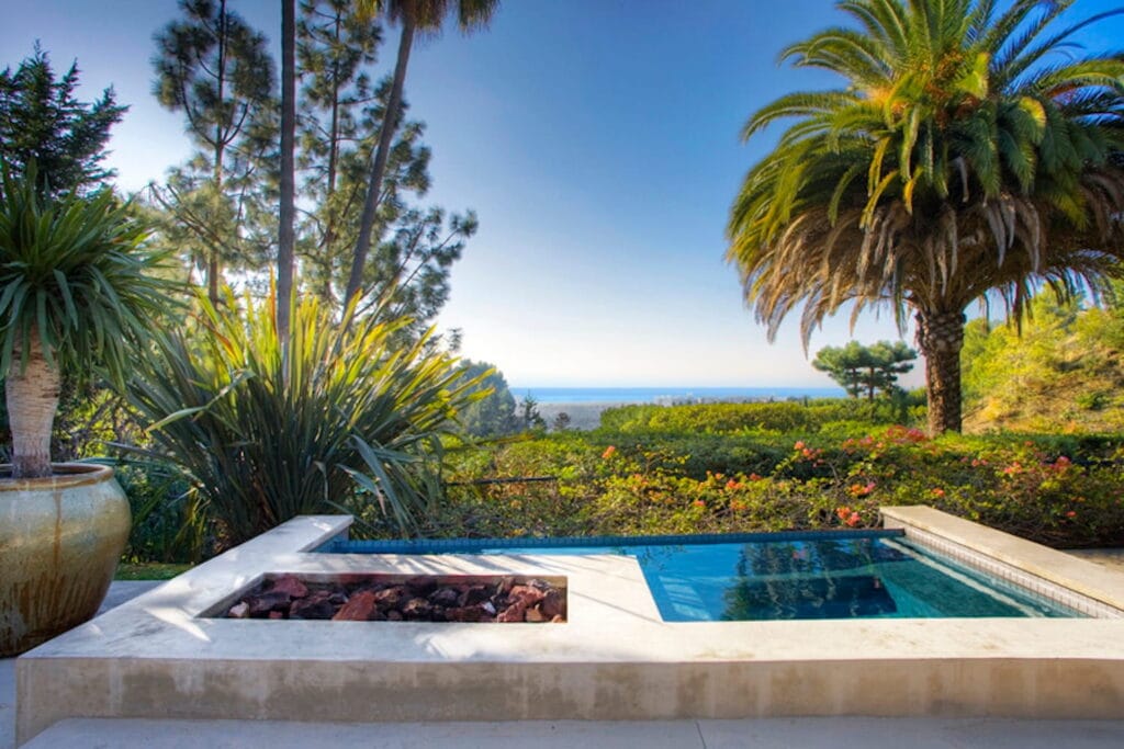 An intimate jacuzzi with a view of the ocean in the distance and palm trees and greenery in the foreground