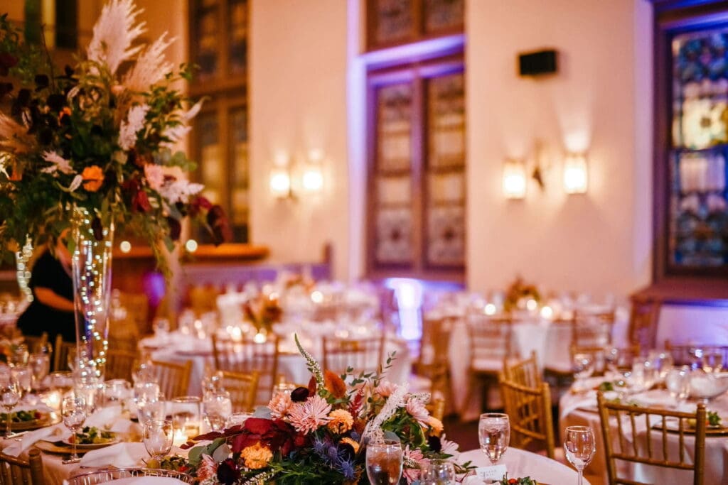 A converted cathedral takes on new life as an event space, decorated for a dinner event with gold chairs, bright flowers, and candlelight.
