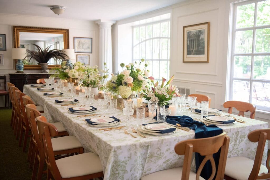 An expansive dining table is set for a party in a brighly-lit traditional dining room