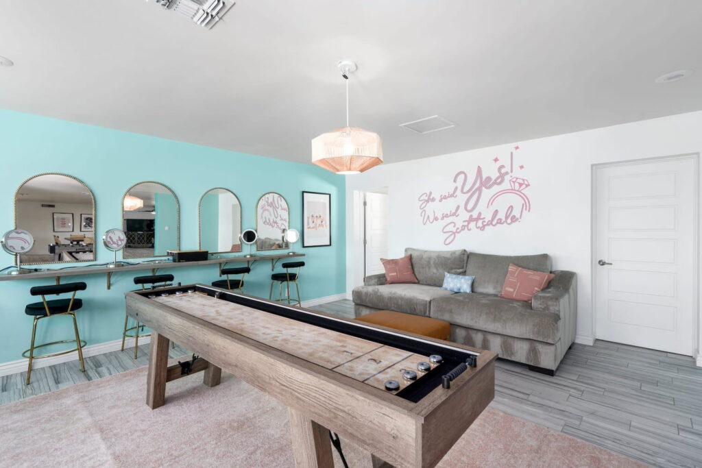 A beauty bar is set up by a shuffle board table in a Phoenix-area home with a "She said Yes, We said Scottsdale" decal on the wall