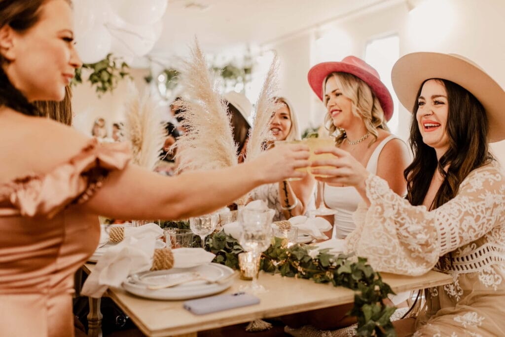 Women toast at an event decorated with bohemian touches like feathers and greenery