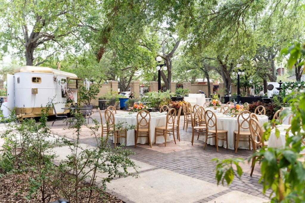 Outdoor reception on a patio surrounded by trees with a small trailer set up as a bar