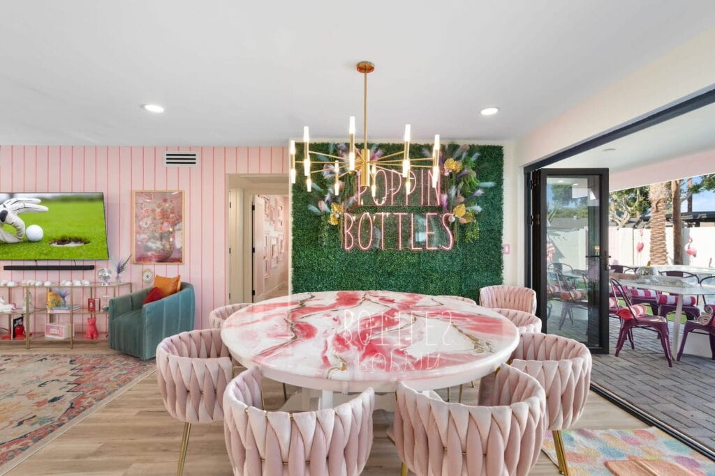 A pink dining and living space in a Phoenix-area home makes for a great bachelorette party pad, complete with outdoor area and neon "Poppin Bottles" sign on the wall